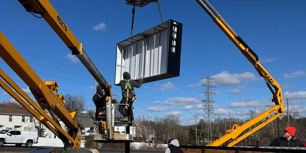 Workers using cranes to lift a large sign.