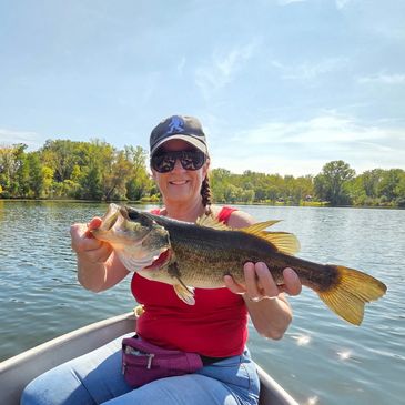 Woman proudly holds a large fish on a boat in a sunny lake.