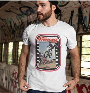 Man wearing a white motocross-themed t-shirt in a graffiti-covered room.