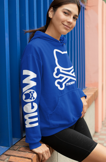 Woman in blue hoodie with cat and bones design leaning on blue wall.