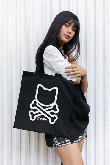 Young woman holding a black tote bag with a cat and crossbones design.