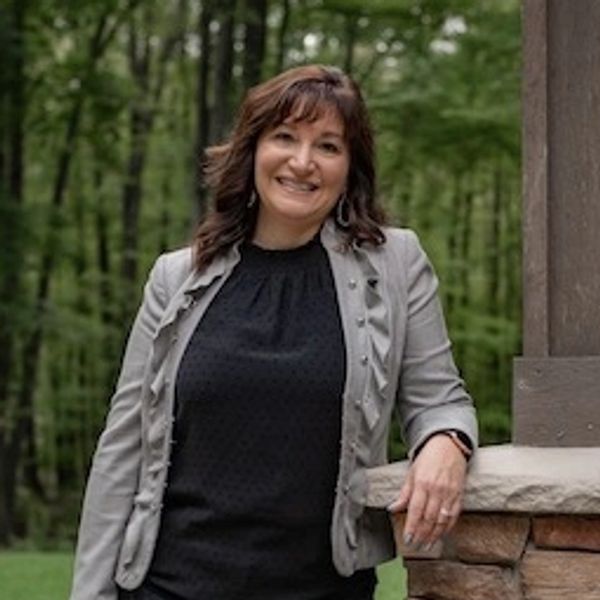 Woman smiling outdoors leaning on stone structure.