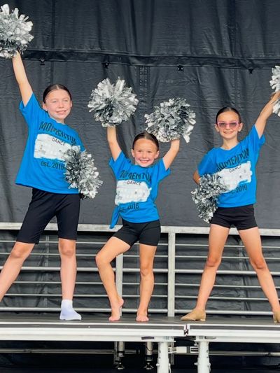 Three young cheerleaders in blue shirts with pom-poms.