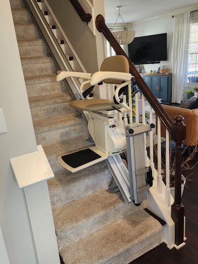 A beige stairlift installed on a carpeted staircase in a home.