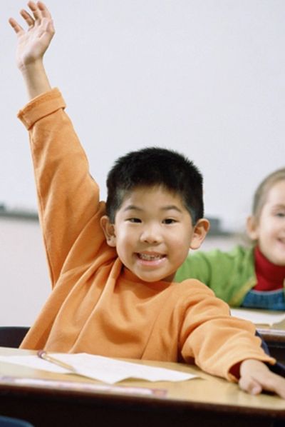 Asian young boy raising hand in a classroom.