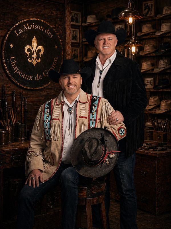 Two men in cowboy hats posing in a rustic hat shop.