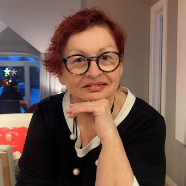 A woman with red hair and glasses smiling indoors.