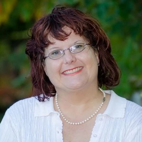 Smiling woman with glasses and pearl necklace outdoors.