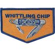 An octagon shaped patch with a pocketknife on it.  Above is WHITTLING CHIP.  It is orange and blue.