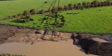 A flooded area adjacent to a green field with trees and bushes.