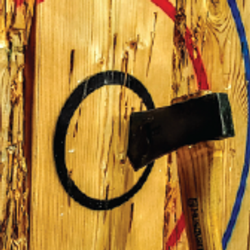 A person throws an axe at a target in our well-lit, safe axe throwing arena.