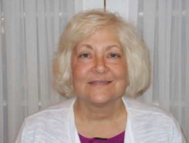 Portrait of a smiling woman with blonde hair against a curtain background.