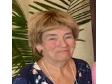 Smiling elderly woman with short blonde hair and floral dress.