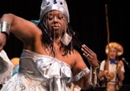 A beautiful woman adorned in a silver dress, headpieces, and jewelry dances on stage. 