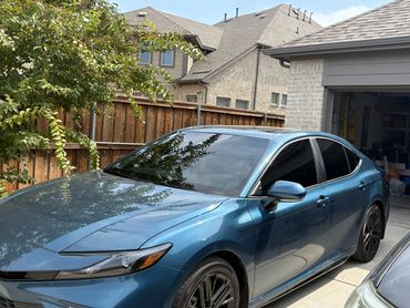 Blue sedan parked in a residential driveway near a wooden fence.