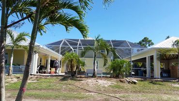 A house with a screened patio and palm trees under a clear blue sky.