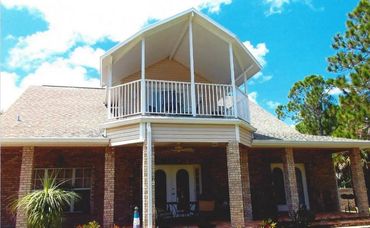 Two-story brick house with a covered balcony and porch under a bright sky.