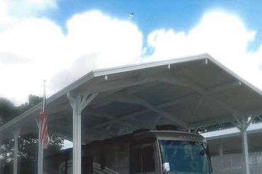 Large RV parked under a covered carport with an American flag nearby.