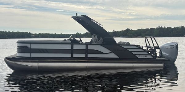 Sleek black and silver pontoon boat floating on calm water at sunset.