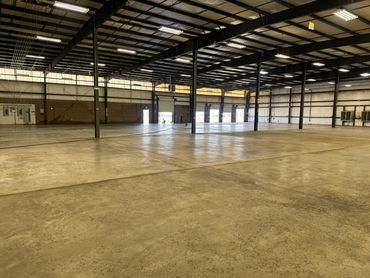 Large empty industrial warehouse with concrete floor and metal beams.