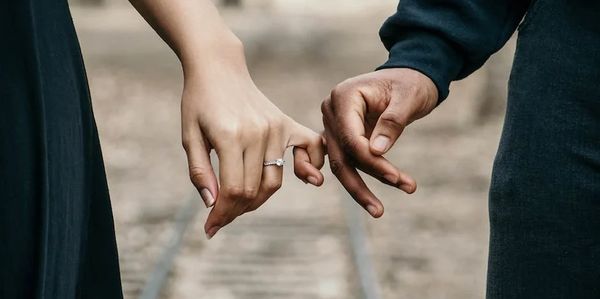Couple interlocking pinky fingers, holding hands.
