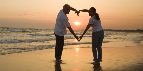 couple on the beach forming a heart with their arms.