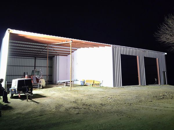 A brightly lit metal shed at night with a man sitting nearby.
