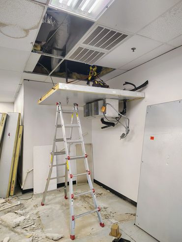 Ladder under a suspended ceiling panel with HVAC unit in a room under renovation.