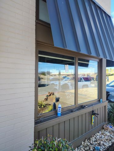 Window cleaning supplies on a building window ledge with reflections of cars and people.