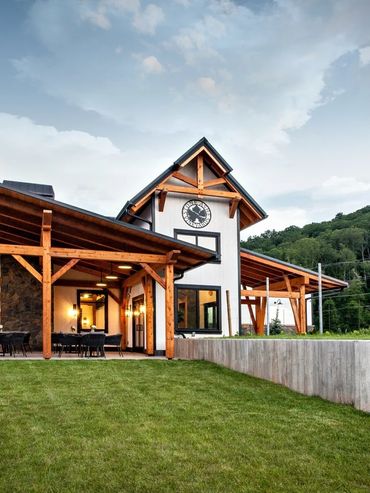 Modern rustic house with wooden beams and outdoor seating under a large roof.