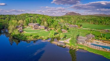 A scenic lakeside resort surrounded by lush greenery and mountains under a partly cloudy sky.