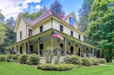 Large yellow house with wraparound porch and American flag.