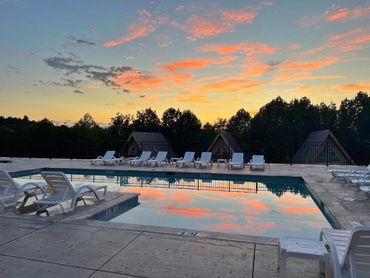 Empty pool area with lounge chairs at sunset reflecting vibrant clouds.