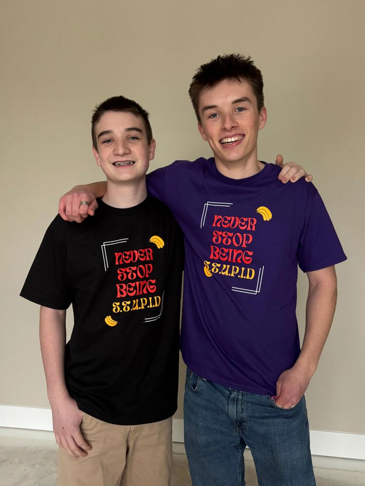 Two young men smiling, wearing matching shirts with the phrase 'Never Stop Being S.T.U.P.I.D'.