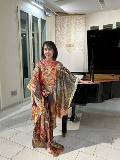 Woman in a colorful flowing dress posing next to a grand piano.