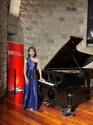Woman in elegant blue dress standing by a grand piano in a stone-walled room.