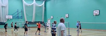 People playing badminton in an indoor gymnasium.