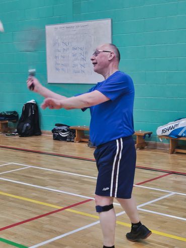 Man playing badminton indoors, mid-action with racket in hand.