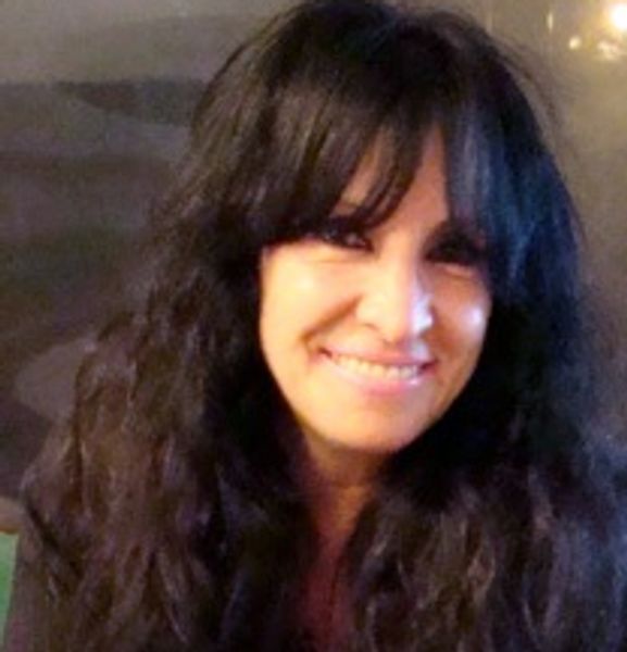 A woman with long curly hair smiling warmly at the camera.