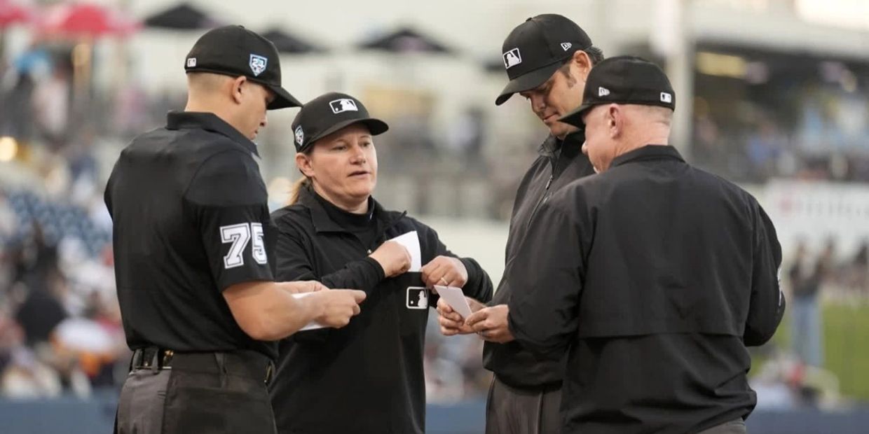 Four baseball umpires in black uniforms confer during a game.