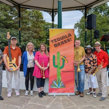 Tequila Brass band poses with instruments in a park gazebo.