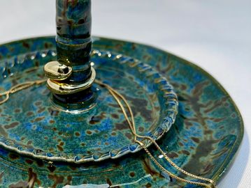 A blue ceramic jewelry holder with rings and a gold chain.
