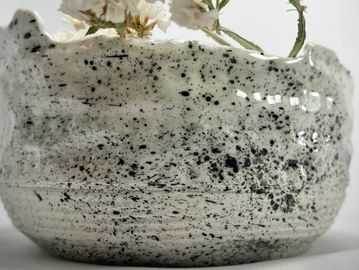 Close-up of a speckled ceramic vase with white flowers.