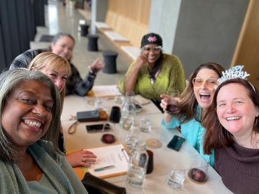 Greer and group of girlfriends sit around the table celebrating a birthday and tasting wine.