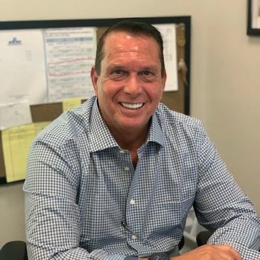 A man smiling warmly while sitting at a desk in an office.