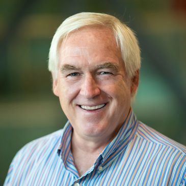 Smiling older man with white hair in a striped shirt.