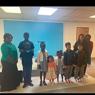 Group photo of diverse children and adults in a room with a blue backdrop.