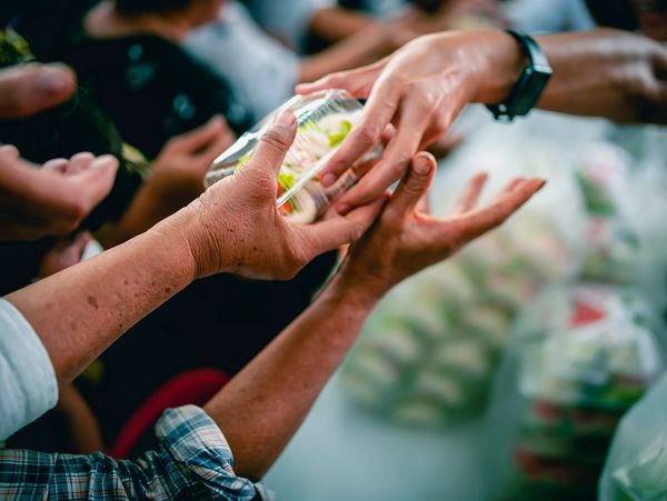 An elderly person's hands reaching out to receive a container of food from another person.