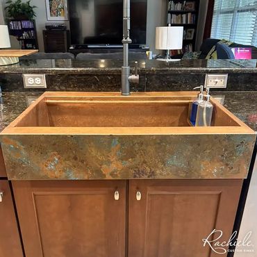copper farmhouse kitchen sink with a custom patina in a dark countertop with wood cabinets
