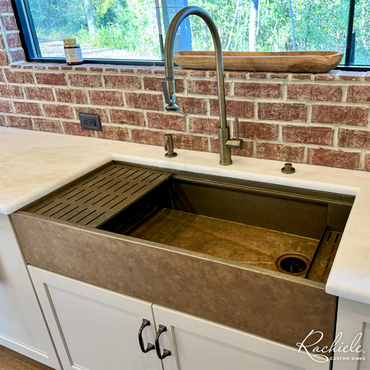 48" bronze farmhouse sink by Rachiele in a rustic kitchen with brick backsplash and Waterstone